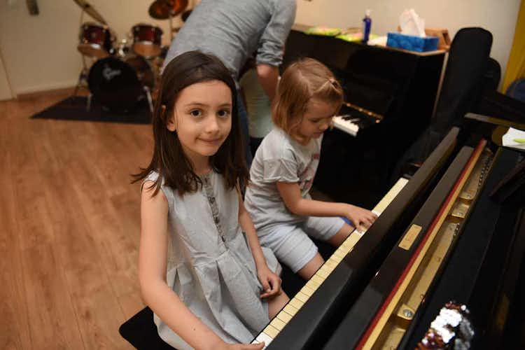 Three children practice piano in a music classroom on two different pianos
