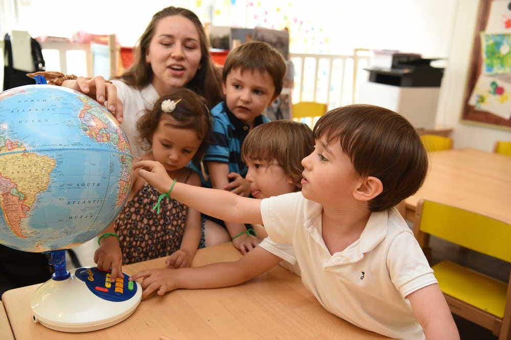 A preschool child points at the globe in a classroom