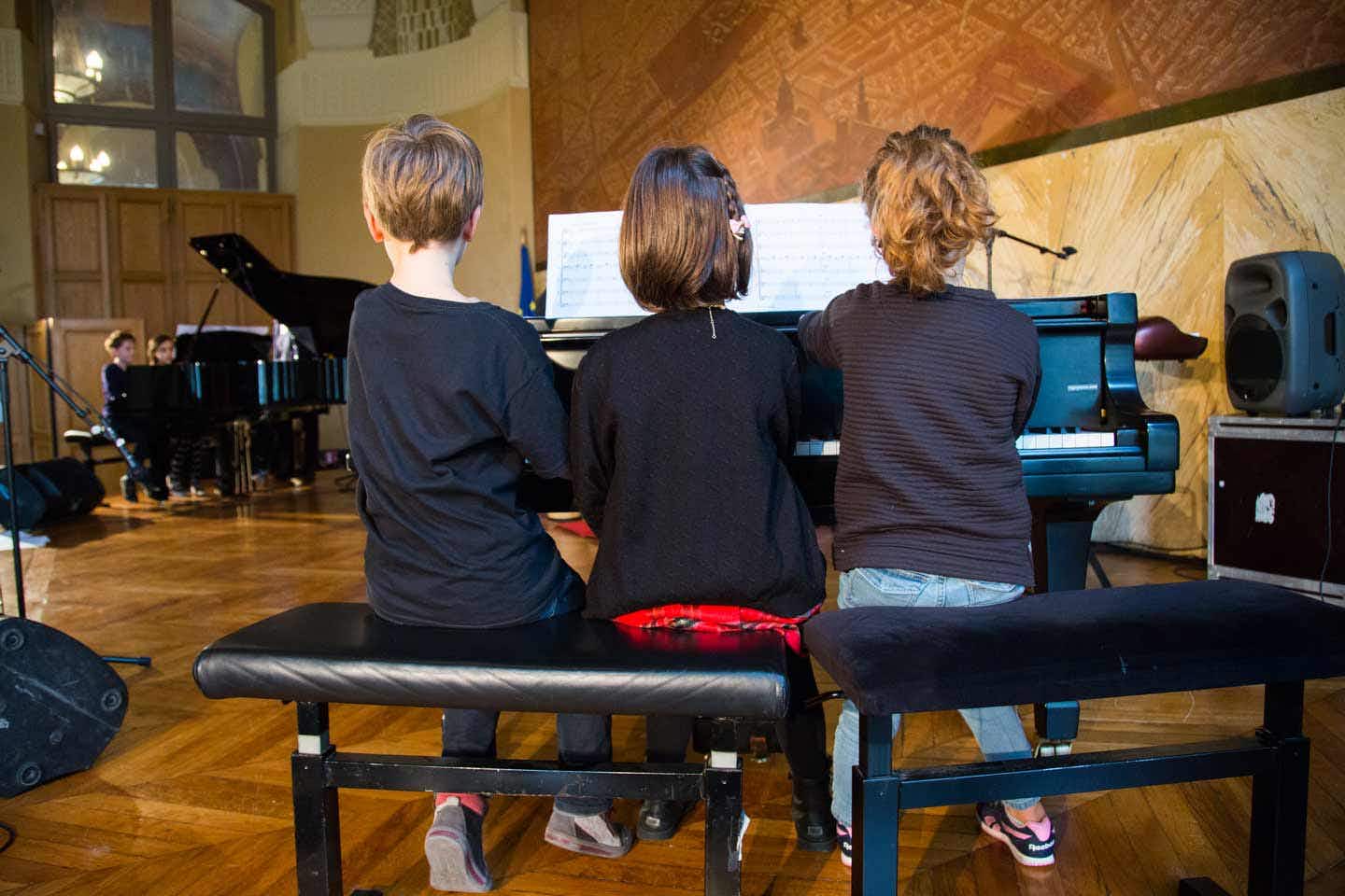 Three children playing piano in a concert hall
