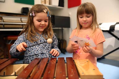 Two children learn how to play xylophone