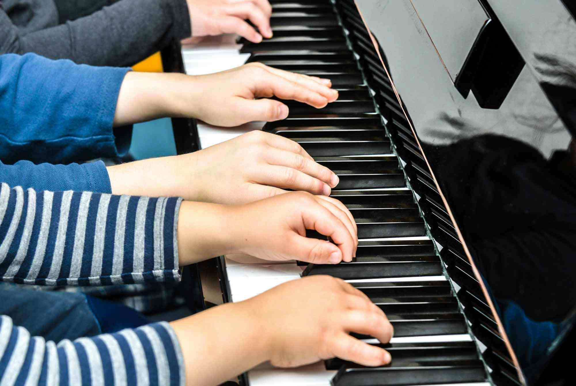 Several children hands on a piano having a music lesson