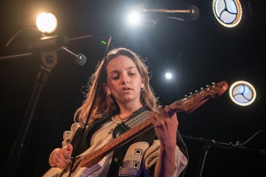 A student girl plays electric guitar in a music venue